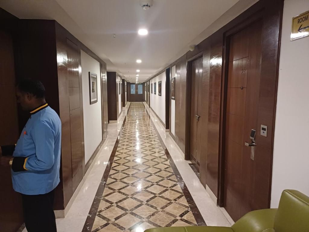 Un couloir d’hôtel avec un sol à motifs, des portes en bois et un panneau indiquant le numéro d’une chambre.