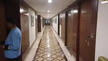 Un couloir d’hôtel avec un sol à motifs, des portes en bois et un panneau indiquant le numéro d’une chambre.