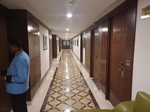 Pasillo de hotel con piso estampado, puertas de madera y un cartel que indica un número de habitación.