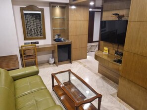 Una sala de estar con un sofá verde, una mesa de centro de madera, un televisor y una pequeña zona de kitchenette.