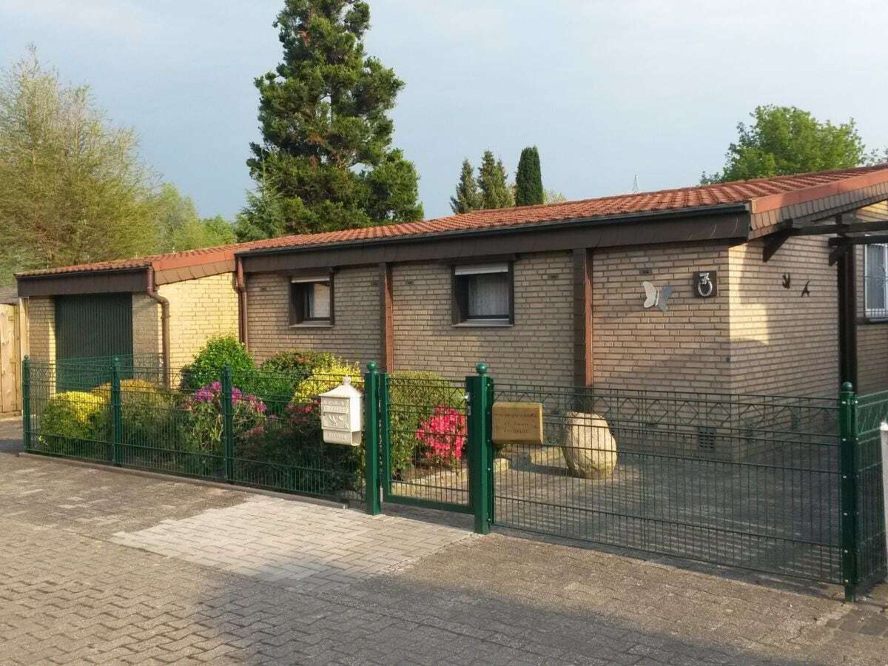 Un bâtiment en briques avec un toit en tuiles, une clôture verte et une boîte aux lettres.