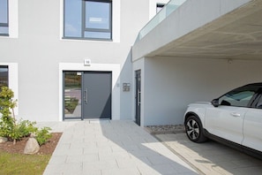 A modern building with a garage door, a white car parked inside, and a paved entrance area. - Second Home Apartment 2 (Lohme)