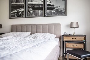 A neatly made bed with a grey headboard, a bedside lamp, and two wicker storage drawers on a nightstand. - Second Home Apartment 2 (Lohme)