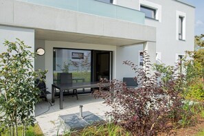 A modern building with a patio area featuring a table and chairs, surrounded by plants and a glass door leading inside. - Second Home Apartment 2 (Lohme)