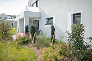 A modern building with a flat roof, large windows, and a well-maintained garden with various plants and shrubs. - Second Home Apartment 2 (Lohme)