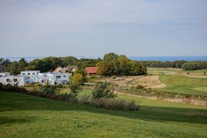 A golf course with a clubhouse, a body of water in the distance, and a hilly landscape. - Second Home Apartment 2 (Lohme)