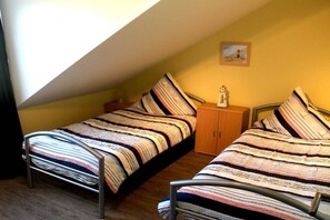 A small, single-room with a sloped ceiling, two beds with striped bedding, a small wooden cabinet, and a framed picture on the wall. - Holiday apartment with 2 bedrooms (Parchtitz)