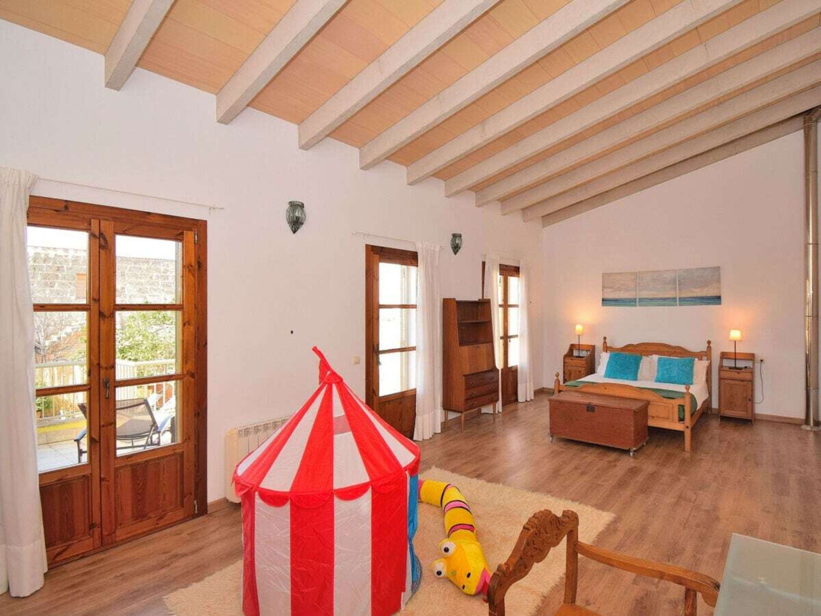 A room with a bed, a wooden chair, a small table, a lamp, and a circus tent.