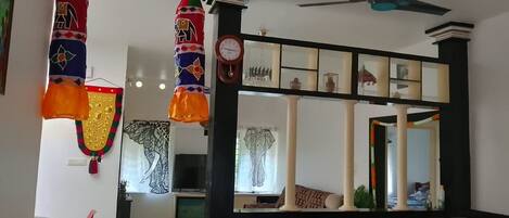 Un salon comprenant un canapé, un fauteuil rouge, un ventilateur de plafond et des objets décoratifs, notamment une horloge et un miroir.
