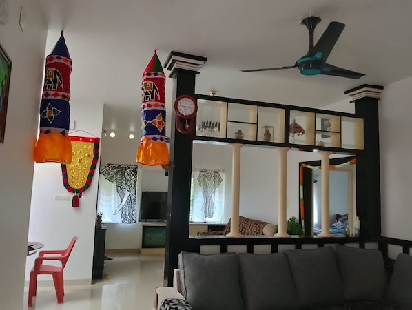 A living room with a sofa, a red chair, a ceiling fan, and decorative items including a clock and a mirror.