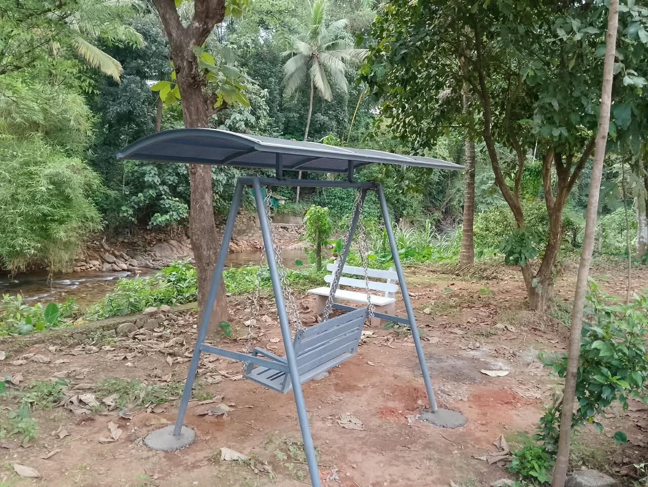 A metal swing set with a bench, surrounded by greenery and a small stream.