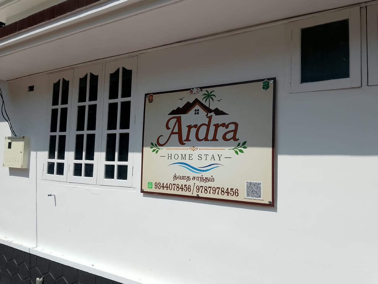 Une enseigne indiquant « Arda Home Stay », avec les numéros de téléphone et un code QR.
