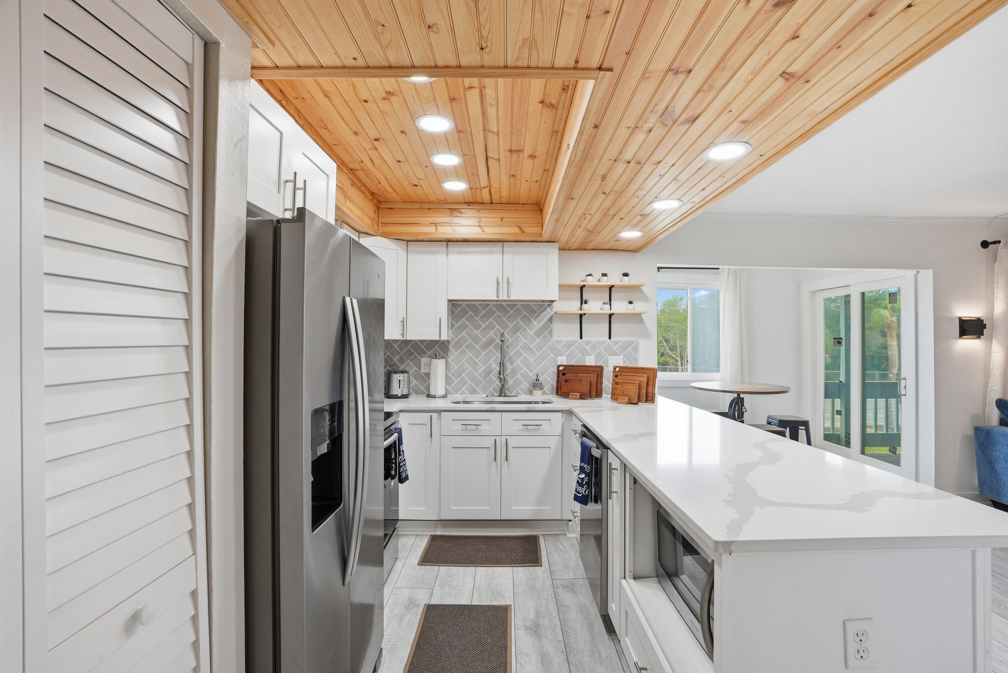 A modern kitchen with a wooden ceiling, white cabinetry, and a large island.