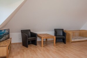 A room with a sloped ceiling, a wooden table, two black chairs, a wooden crib, and a television on a wooden stand. - Holiday home with 3 bedrooms (Heringsdorf)