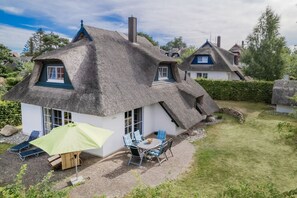 A thatched-roof house with a patio area, outdoor seating, and a visible garden. - Holiday home with 3 bedrooms (Heringsdorf)