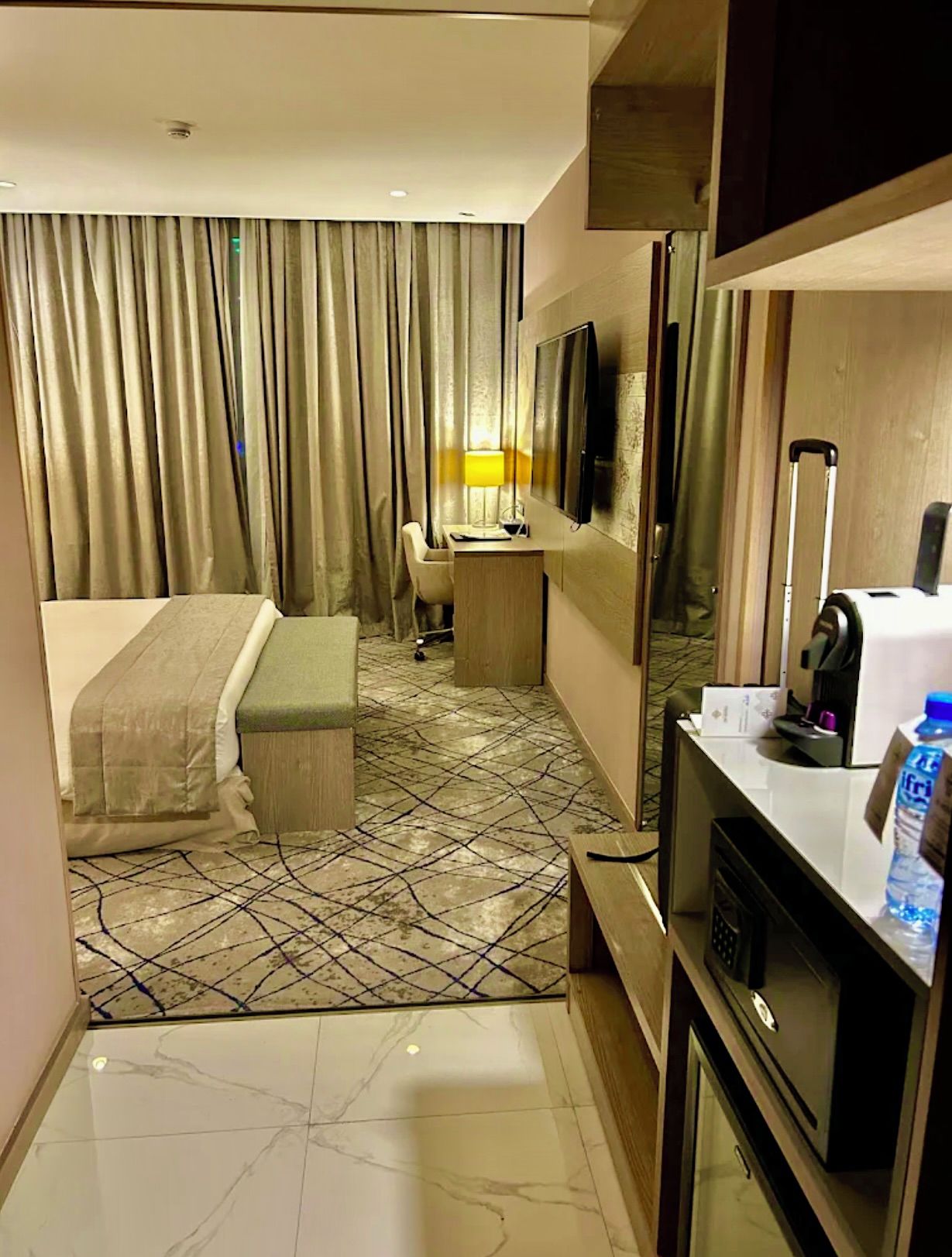 Habitación de hotel con una cama, un escritorio con silla, televisor, microondas y una botella de agua.