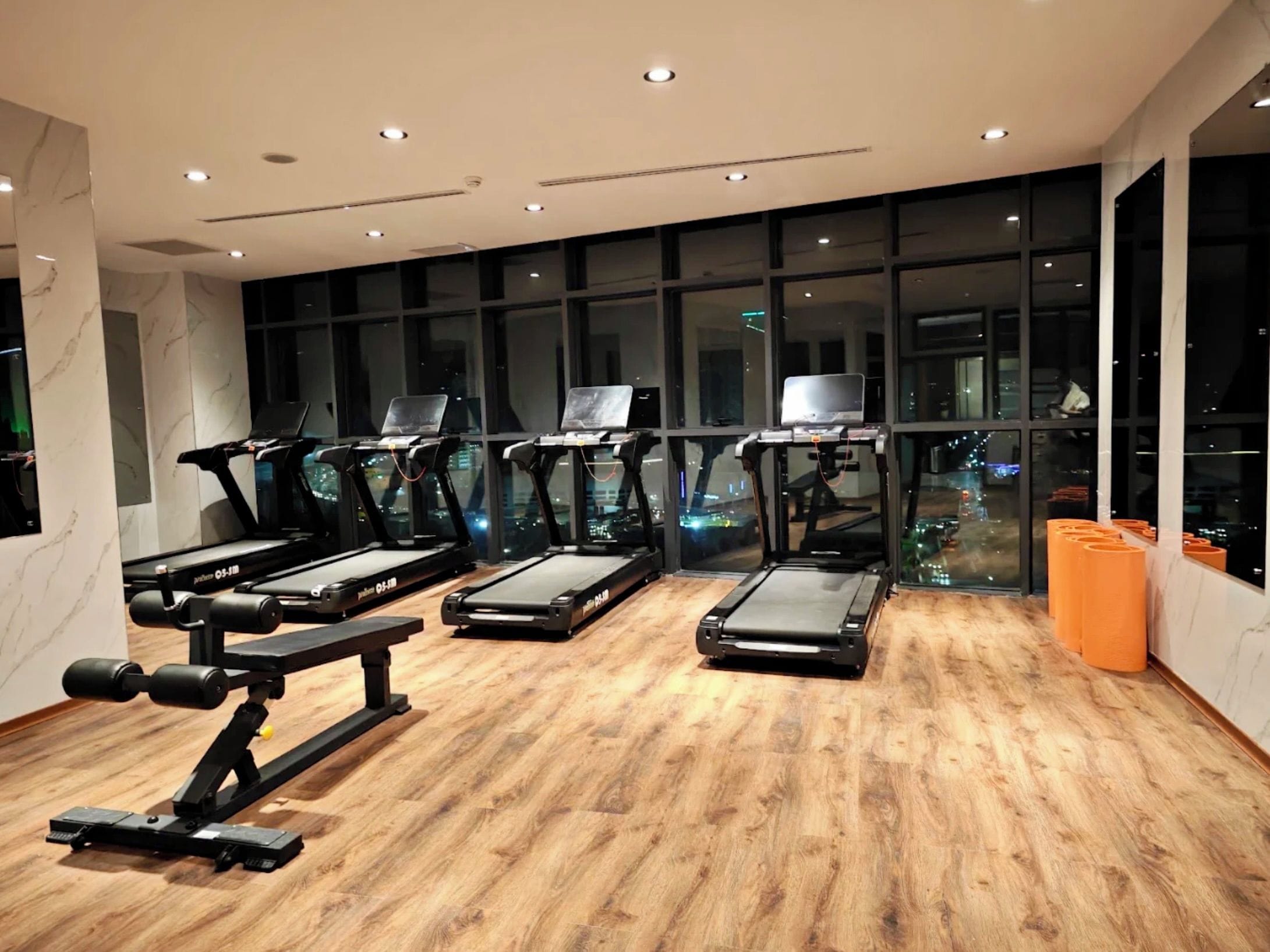 A gym with treadmills, weight machines, and a large window with a city view.