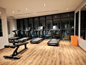Un gimnasio con cintas de correr, máquinas de pesas y un amplio ventanal con vista a la ciudad.