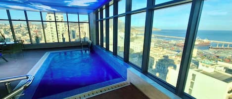 Una piscina interior con vista a la ciudad, grandes ventanales y un techo con diseño de nubes.