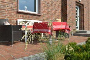 An outdoor seating area with a brick building in the background, a table covered with a red and white tablecloth, and a chair with a cushion. - Holiday apartment with 2 bedrooms (Breege)