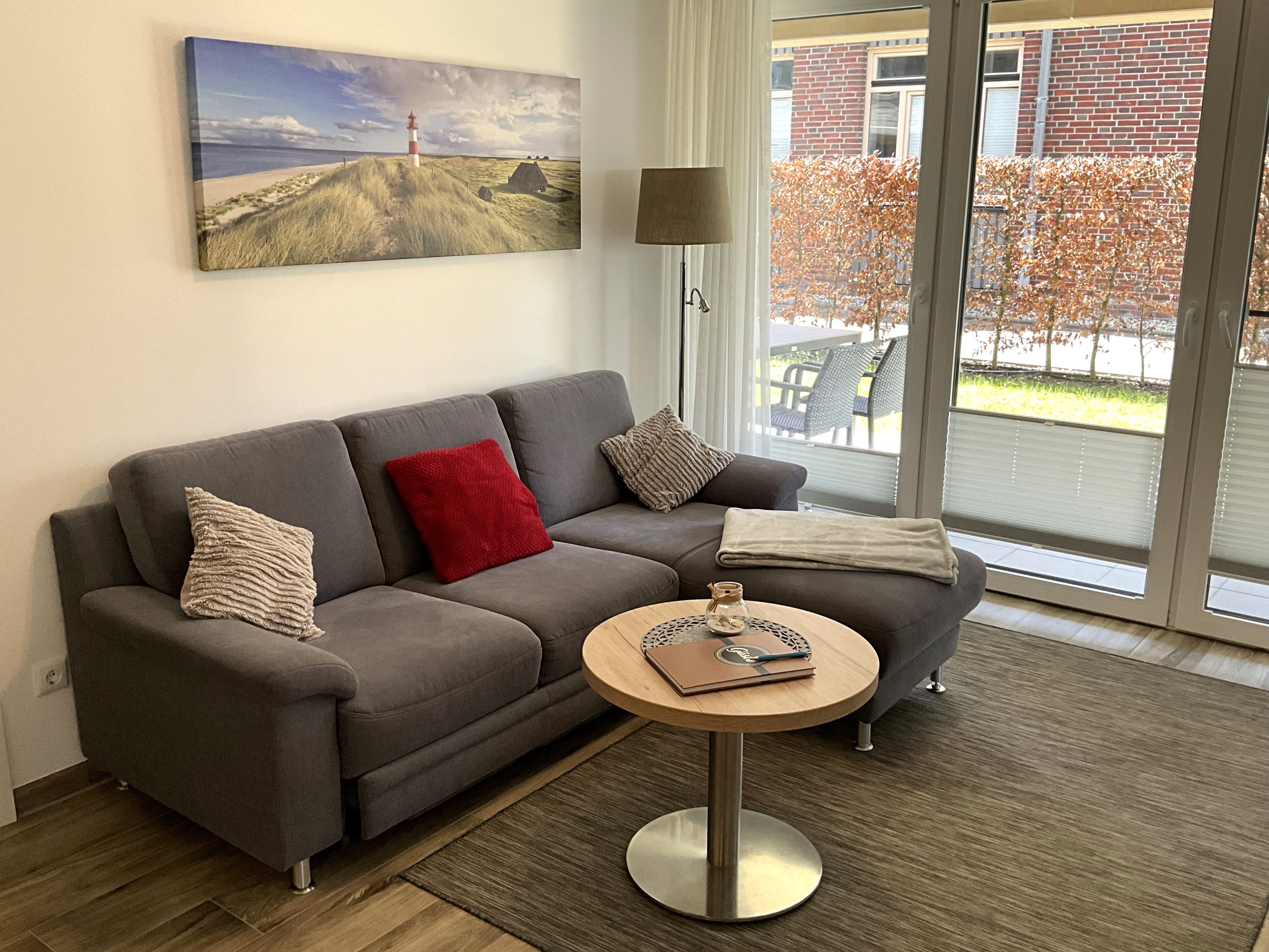 Ein modernes Wohnzimmer mit einem grauen Sofa, einem runden Holztisch und einem Gemälde mit einer Strandansicht.