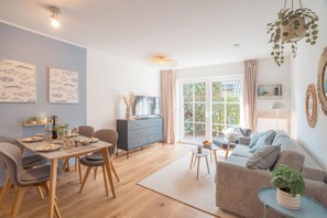 A modern living room with a sofa, a dining table set for two, and a television. - Hi there, and welcome to the Küstenkoje! (Dangast)