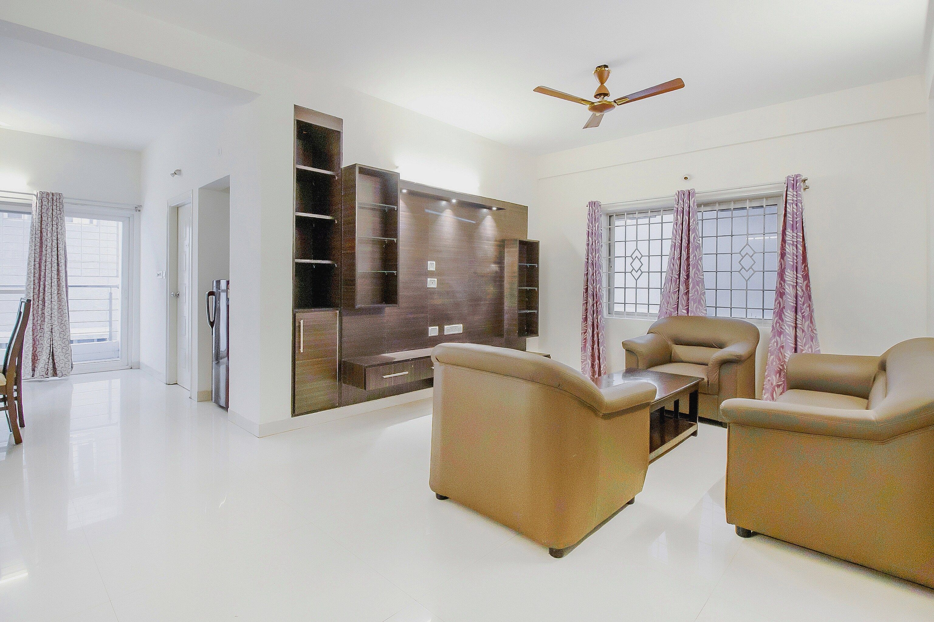 A spacious living room with a flat-screen TV, two sofas, a coffee table, and a ceiling fan.