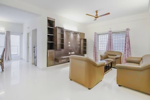 A spacious living room with a flat-screen TV, two sofas, a coffee table, and a ceiling fan.