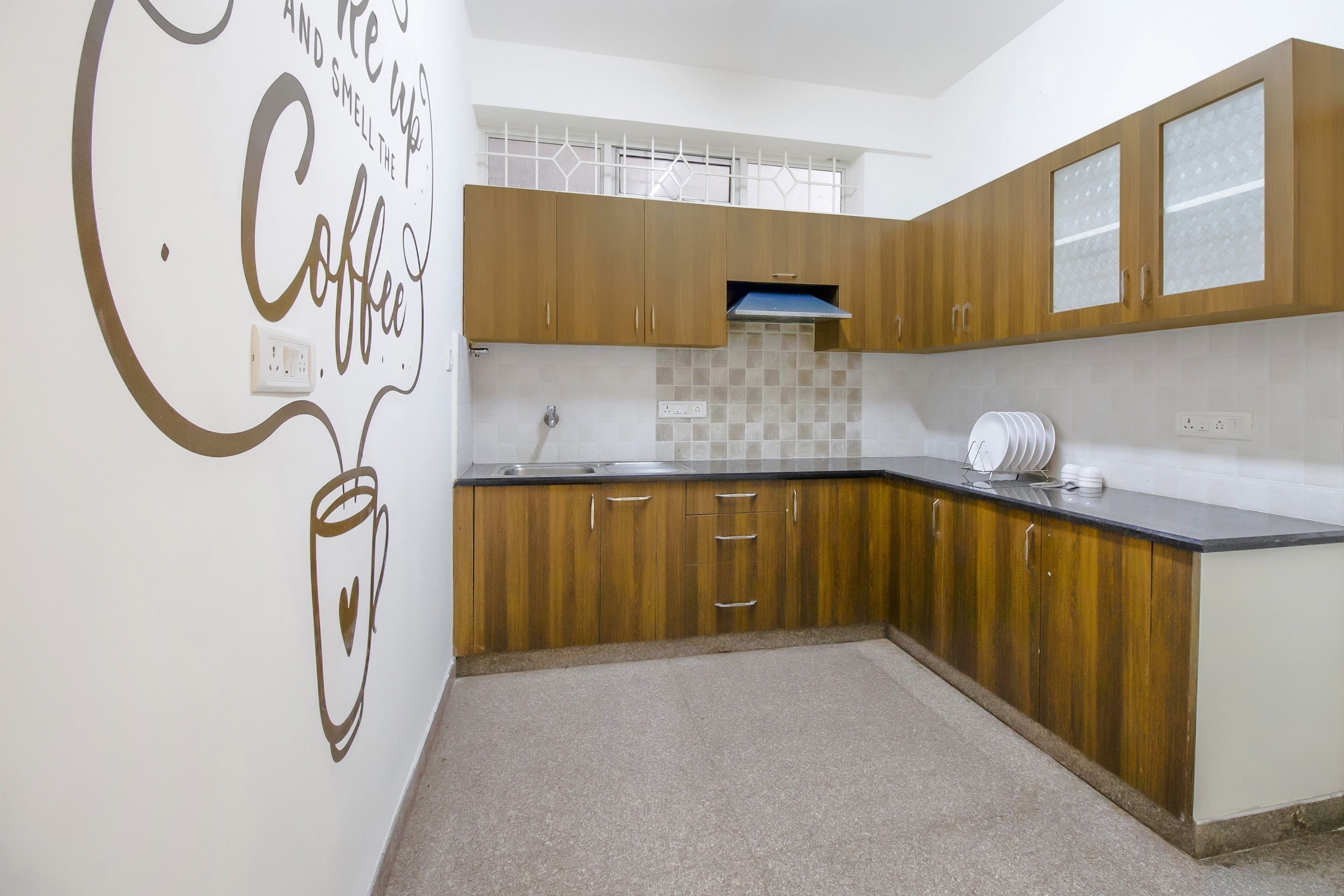 A kitchen with wooden cabinets, a countertop, and a wall with a coffee-themed design.