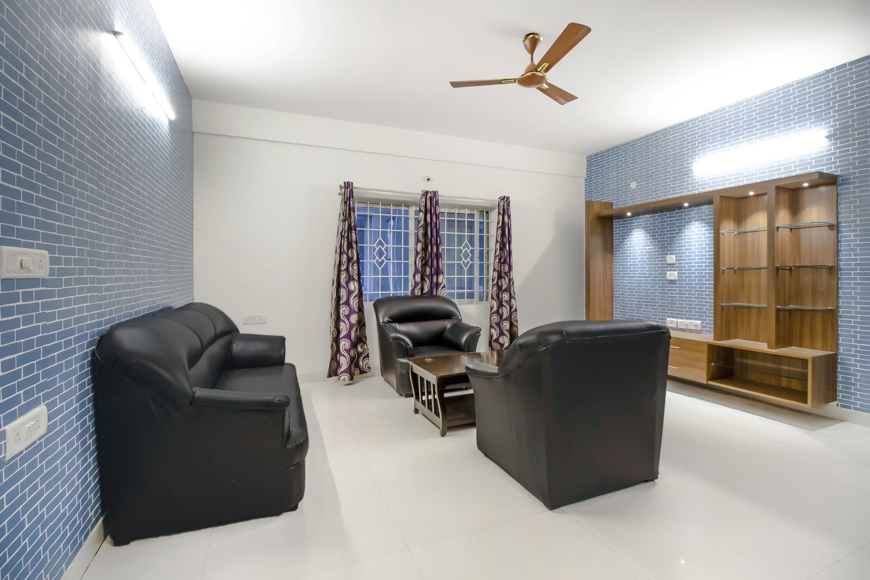 A room with a brick-patterned wall, a ceiling fan, a window with patterned curtains, and a wooden cabinet with shelves.
