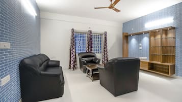 A room with a brick-patterned wall, a ceiling fan, a window with patterned curtains, and a wooden cabinet with shelves.