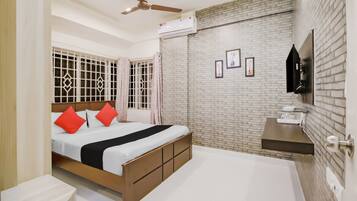 A bedroom with a bed, a ceiling fan, an air conditioning unit, a brick wall, and a mounted TV.