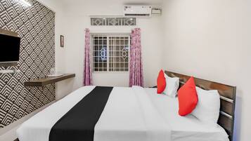 A hotel room with a bed, a TV, an air conditioning unit, and a window with curtains.