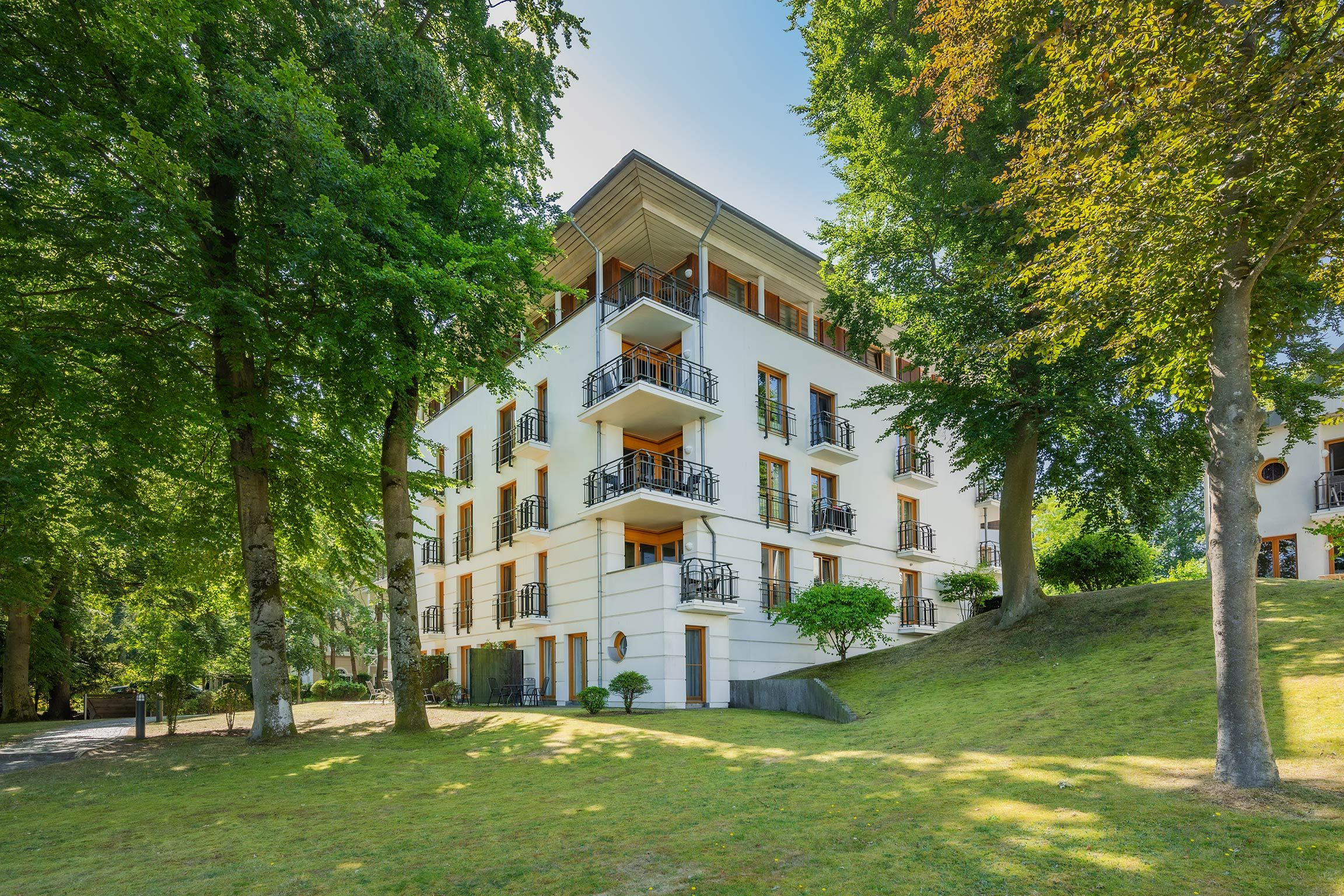 A multi-story hotel with balconies, surrounded by trees and a grassy area.