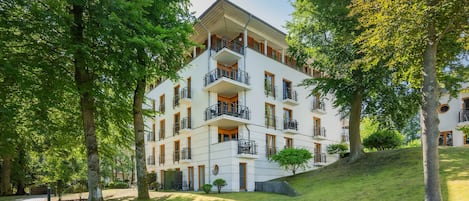 A multi-story hotel with balconies, surrounded by trees and a grassy area.