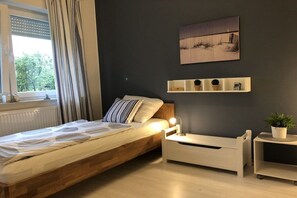 Ein Schlafzimmer mit einem hölzernen Bett, Nachttischen, einem Fenster mit Vorhängen, einem Wandregal mit Dekoration und einem Gemälde.