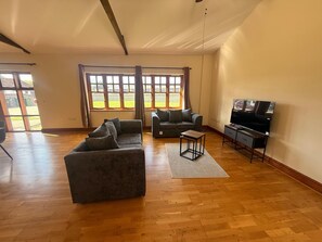 A spacious living room with a large window, a sofa, a coffee table, and a TV stand. - 1 BlackDyke 3 bedroom house with garden (Hockwold cum Wilton)