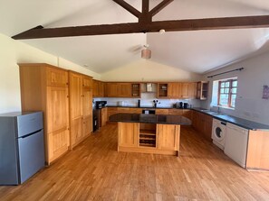 A kitchen with wooden cabinets, a central island, a washing machine, and a built-in oven. - 1 BlackDyke 3 bedroom house with garden (Hockwold cum Wilton)