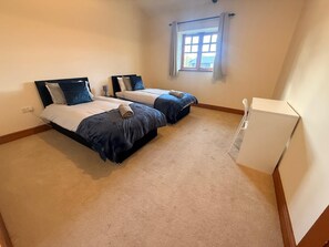 A bedroom with two beds, a window with curtains, and a white chair. - 1 BlackDyke 3 bedroom house with garden (Hockwold cum Wilton)