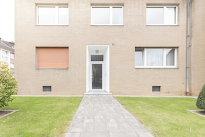 A two-story brick building with a central entrance, a small garden area, and a paved walkway leading to the door. - Vrbo Property (Meerbusch)