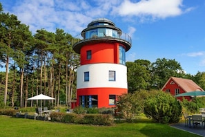 A red and white lighthouse with a circular observation deck, surrounded by a well-maintained garden and a red house. - Holidays in a Lighthouse (Glowe)