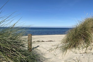 A beach with sand, grass, and a wooden post. - Holidays in a Lighthouse (Glowe)