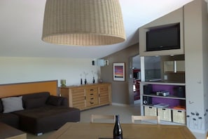 Ein modernes Wohnzimmer mit einer Couch, einem Esstisch mit einer Flasche, einem Fernseher und einem Bücherregal.