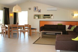 A living room with a sofa, a dining table with chairs, a hanging light fixture, and a flat-screen TV mounted on the wall. - Holiday home with 4 bedrooms (SAINT MICHEL D'EUZET)