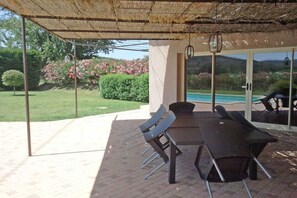 An outdoor patio with a table and chairs, a pool in the background, and a view of a garden with pink flowers. - Holiday home with 4 bedrooms (SAINT MICHEL D'EUZET)