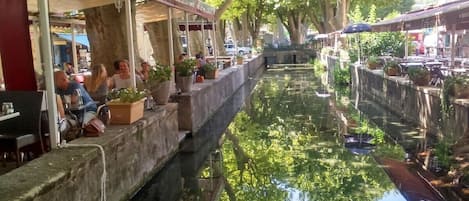A canal-side restaurant with outdoor seating, a waterway, and trees.