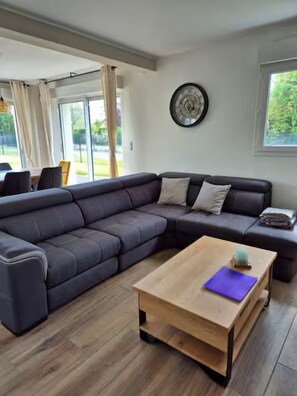 Un salon moderne avec un canapé d’angle, une table basse en bois et, au fond, un coin repas.