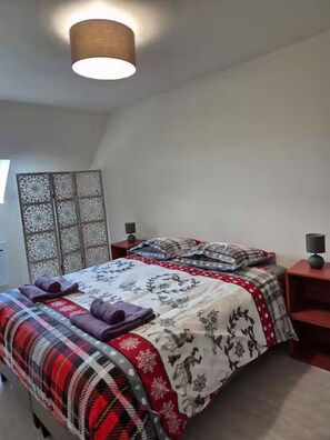 Une chambre à coucher comprenant un lit, une table de chevet, une lampe et un élément de séparation décoratif.