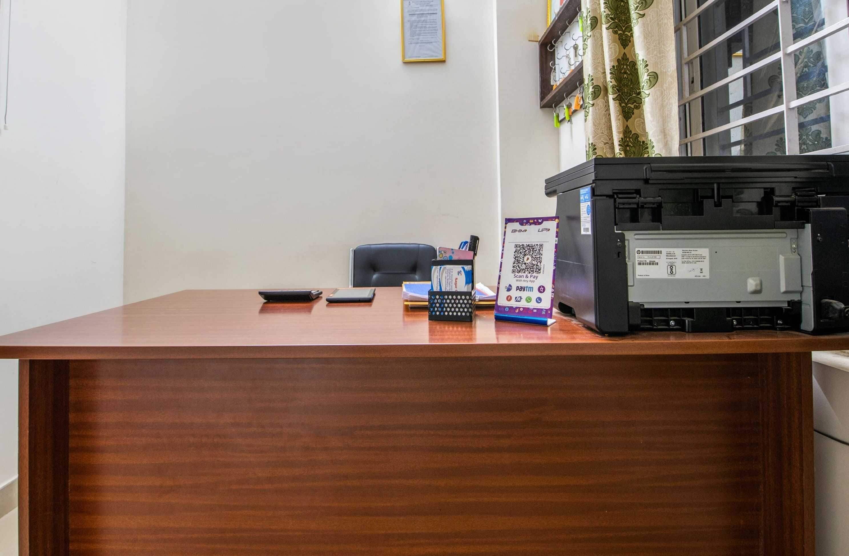 A wooden desk with a printer, a smartphone, a tablet, and a QR code payment sign.