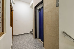 Corredor com porta azul, corrimão e piso de azulejos.